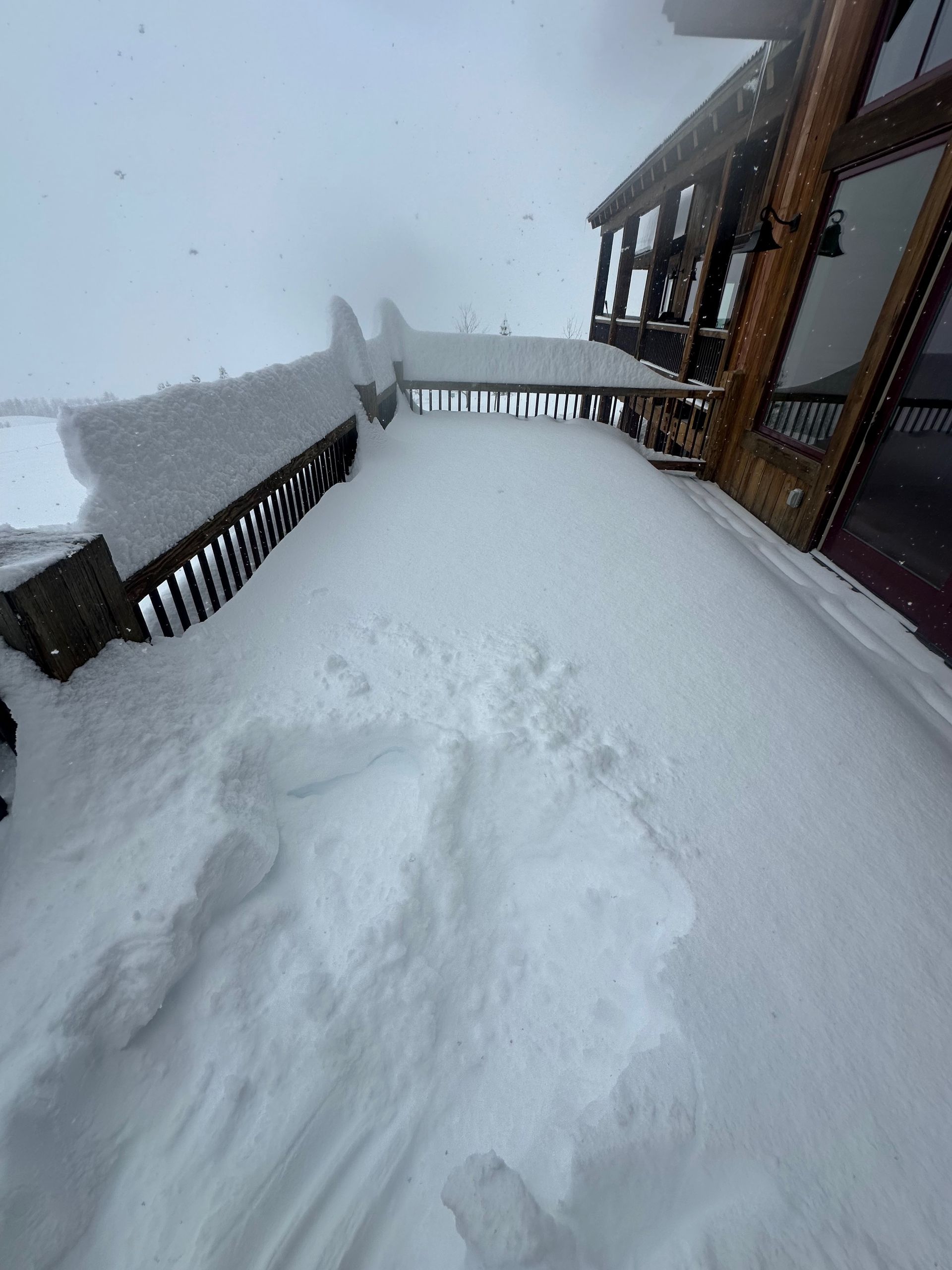 Snow-covered deck next to a building with wooden trim, overcast sky.