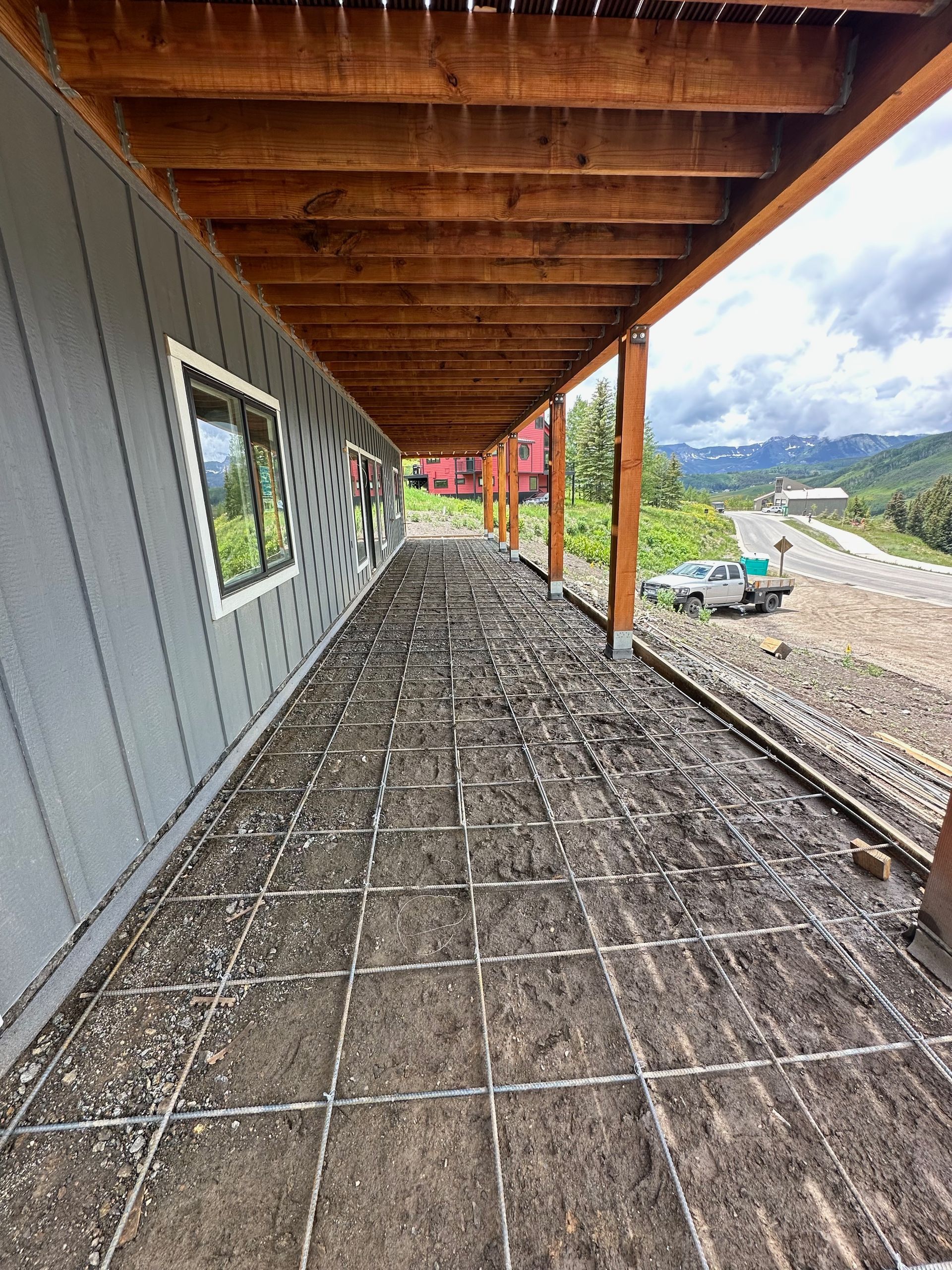 Construction site: porch with wire mesh on the ground, wooden beams above, and a view of mountains and road.