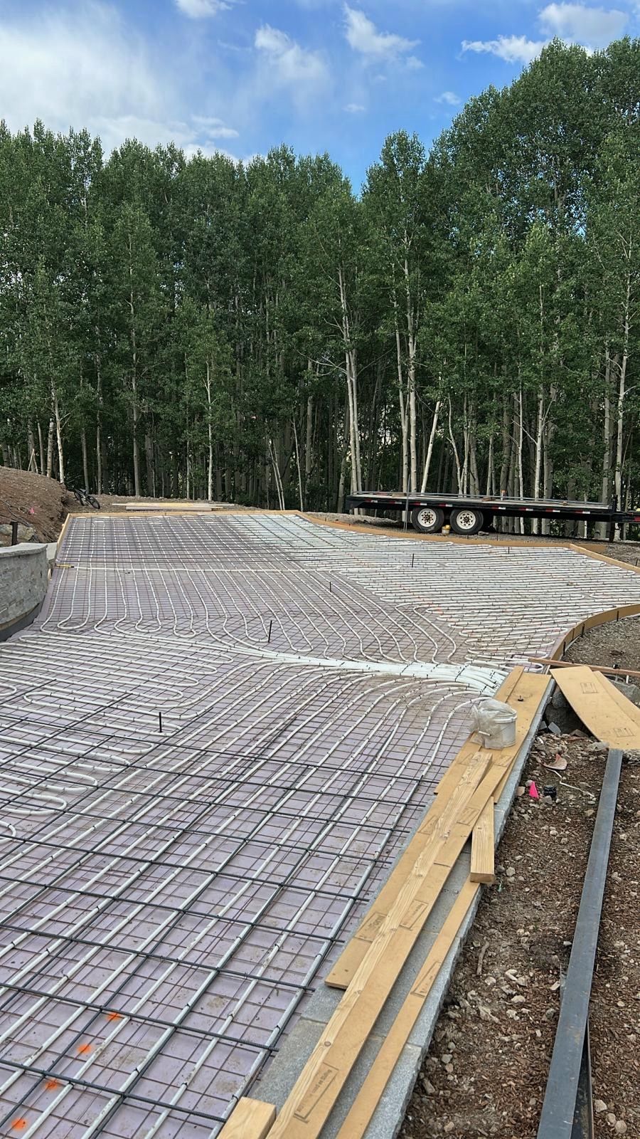 Construction site with rebar grid prepared for concrete driveway; woods in background.