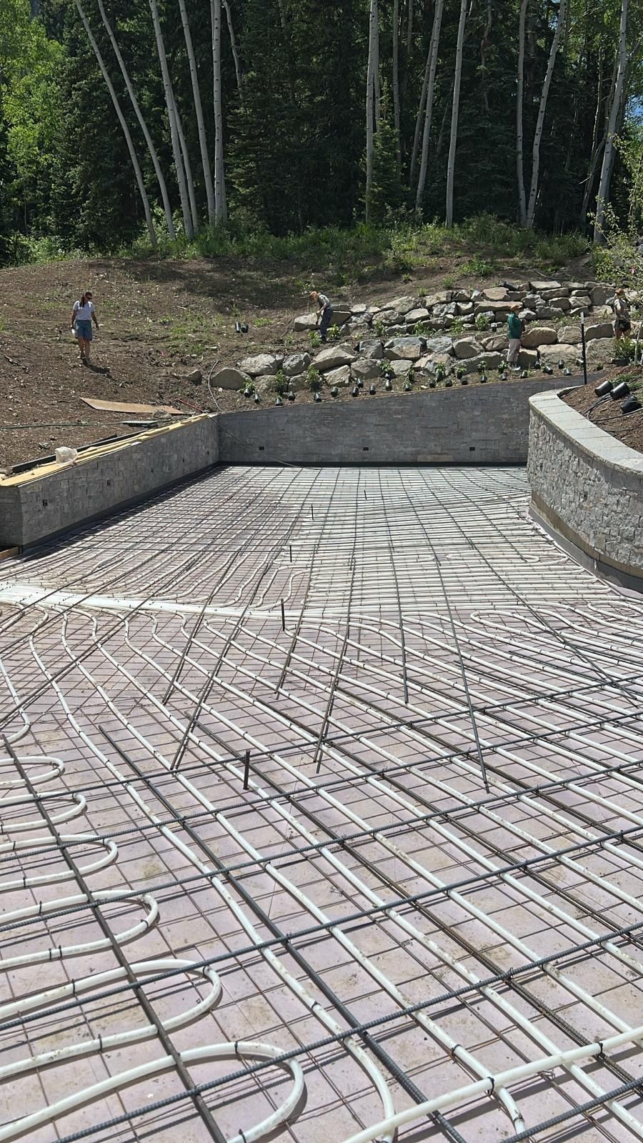 Concrete driveway with embedded radiant heat tubing, surrounded by stone walls. A person stands on a hill.