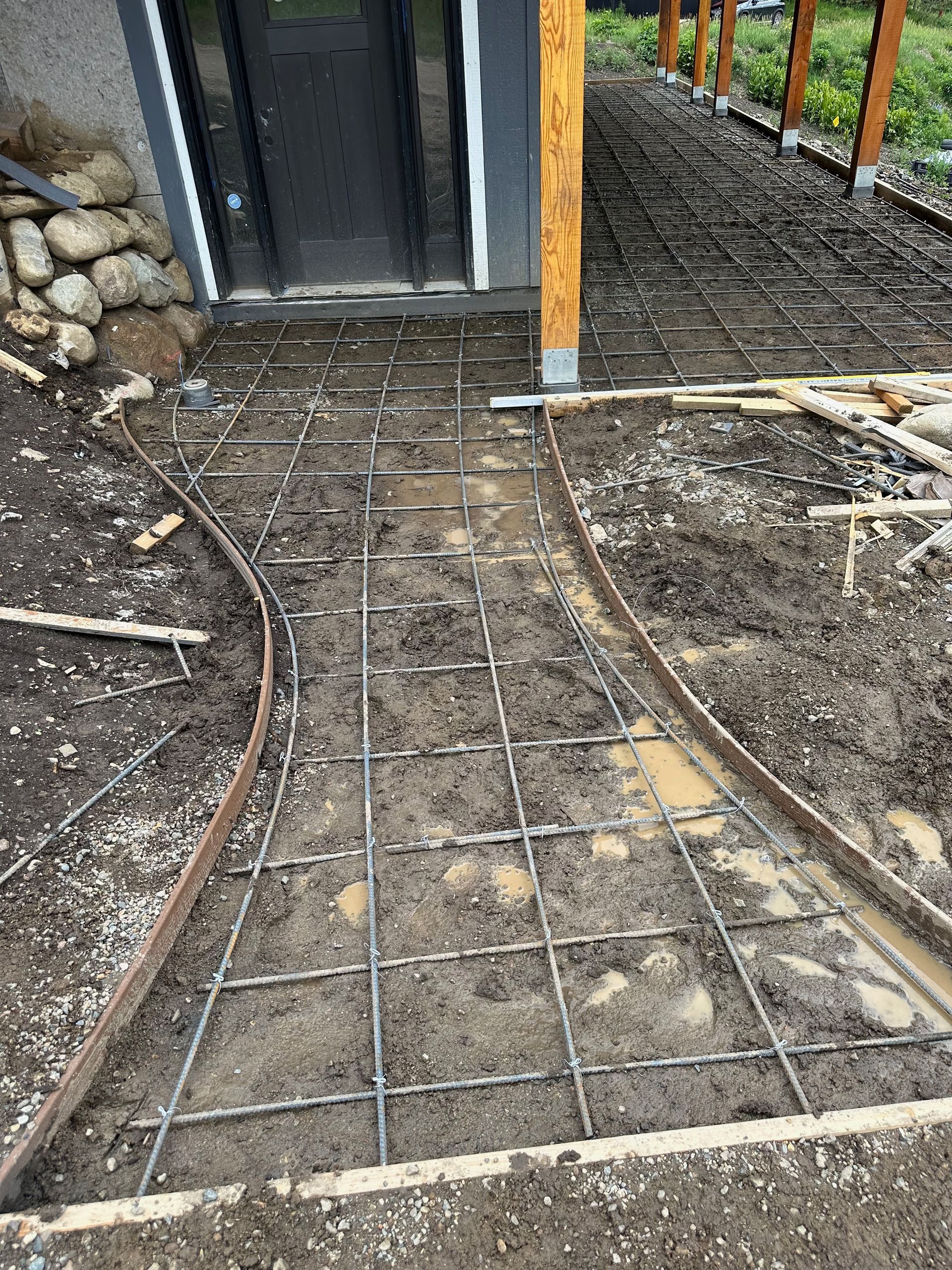 Pathway under construction, rebar grid within curved metal edging, muddy ground.