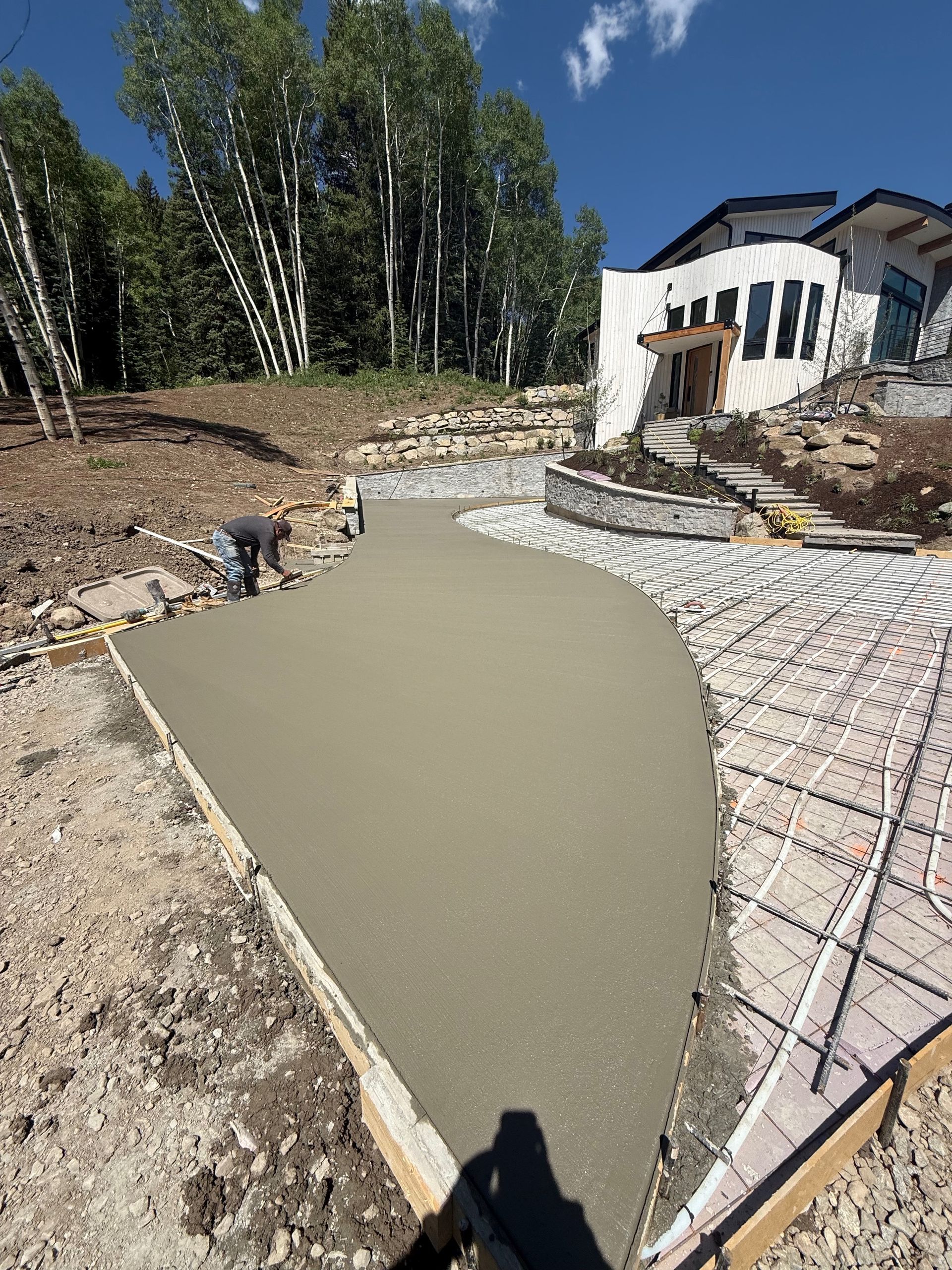 Freshly poured concrete pathway with a person working; next to a patterned walkway and house.