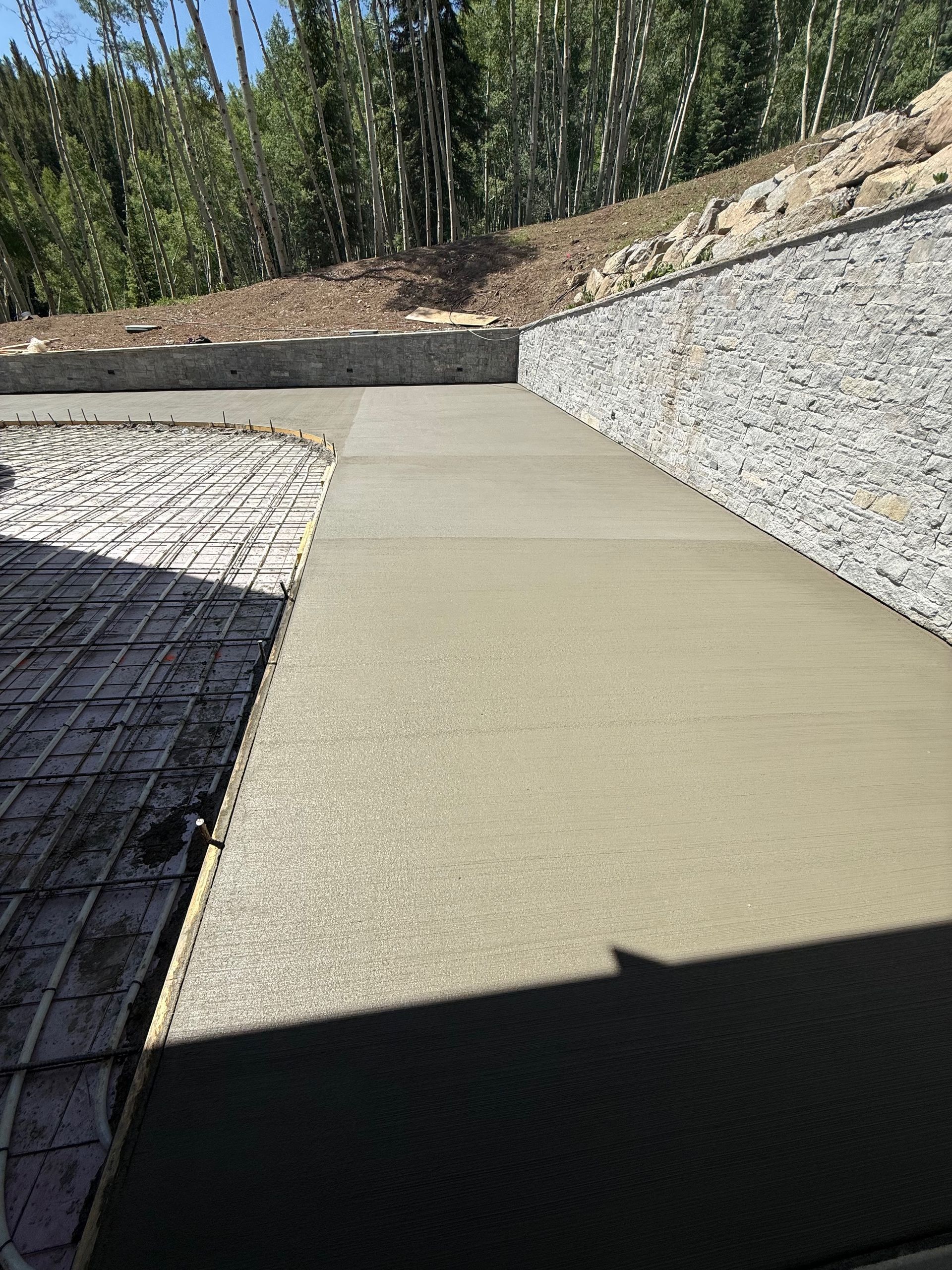 Freshly poured concrete walkway next to a gravel retaining wall, with rebar visible on the left.