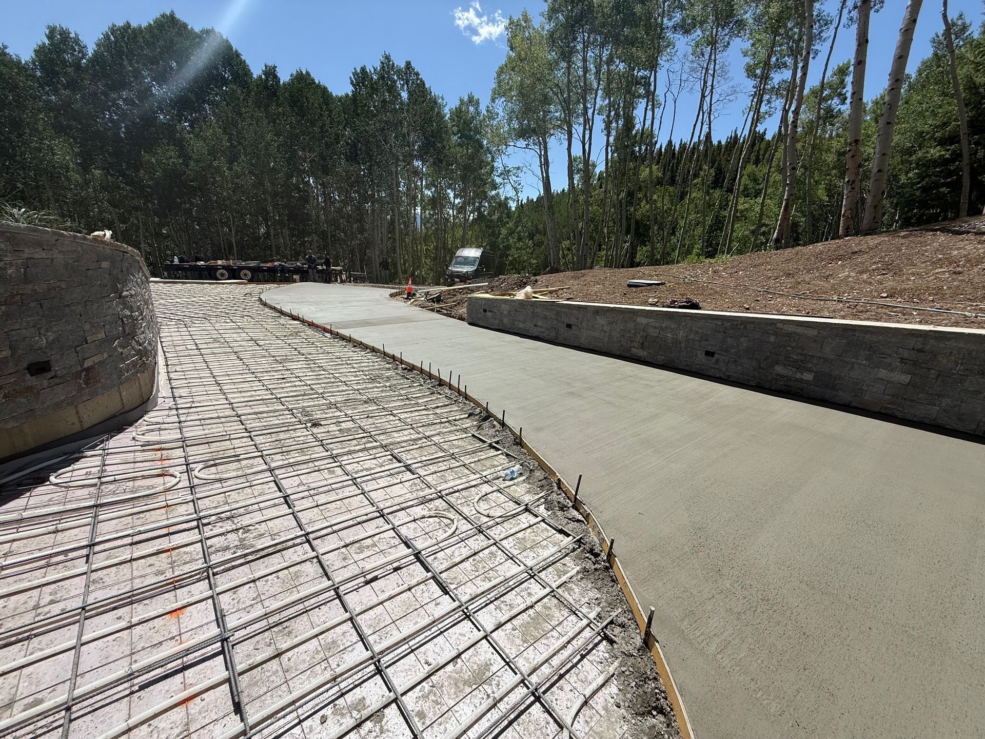Concrete driveway under construction with rebar and fresh concrete. Sunny outdoor setting.