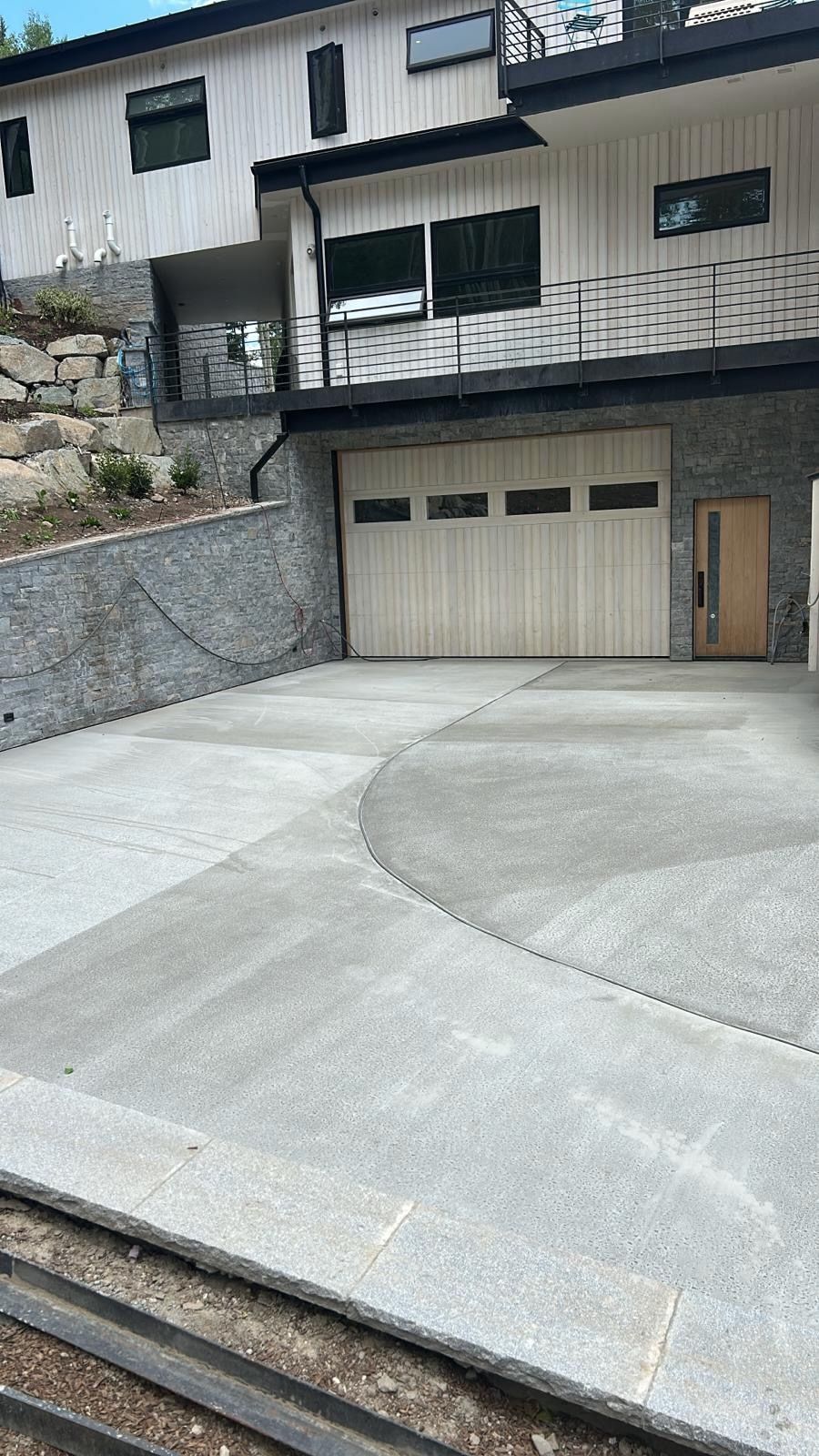 Driveway leading to a modern house with a light wooden garage door and stonework.