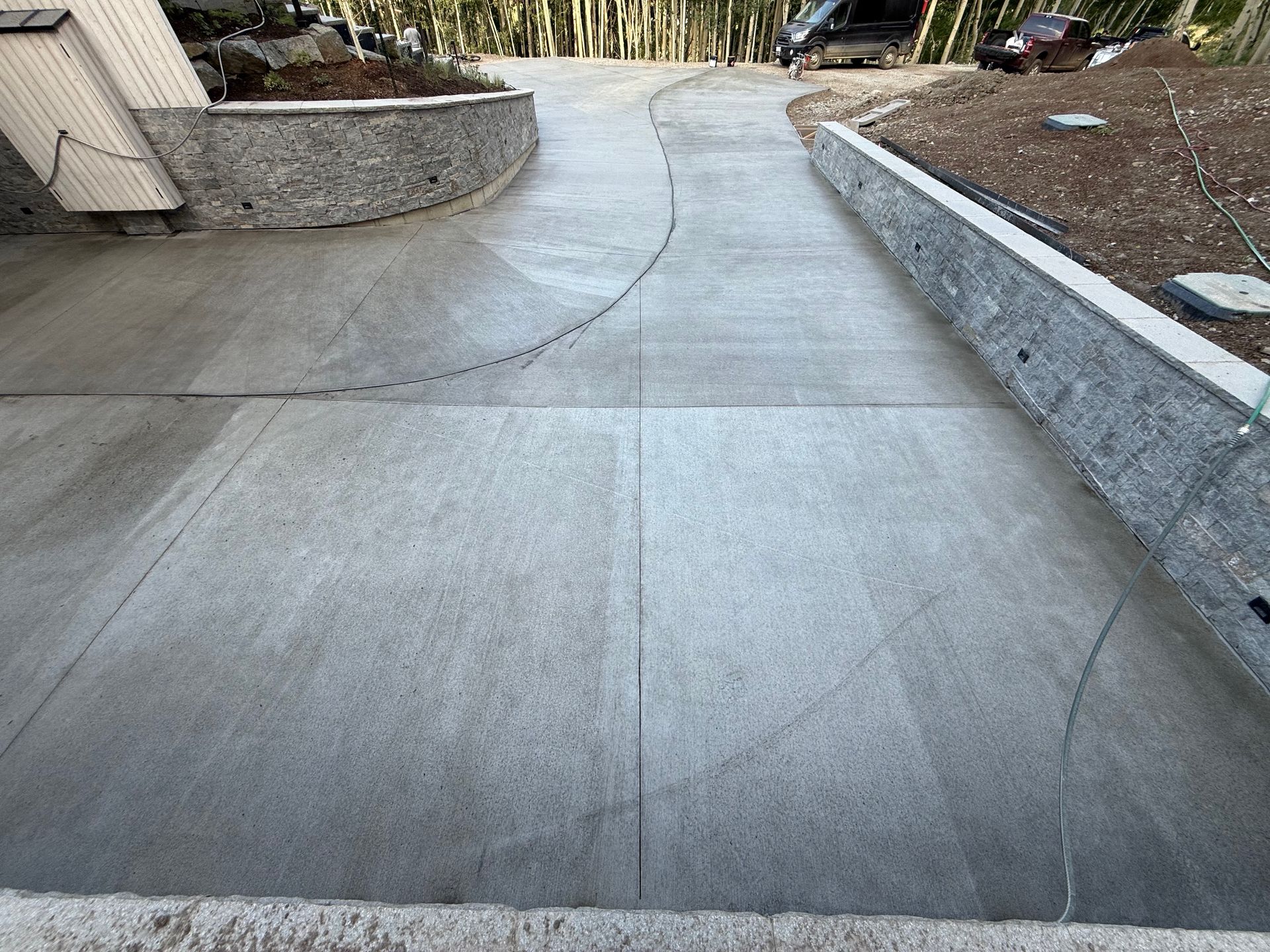 Concrete driveway curving uphill, flanked by stone retaining walls.