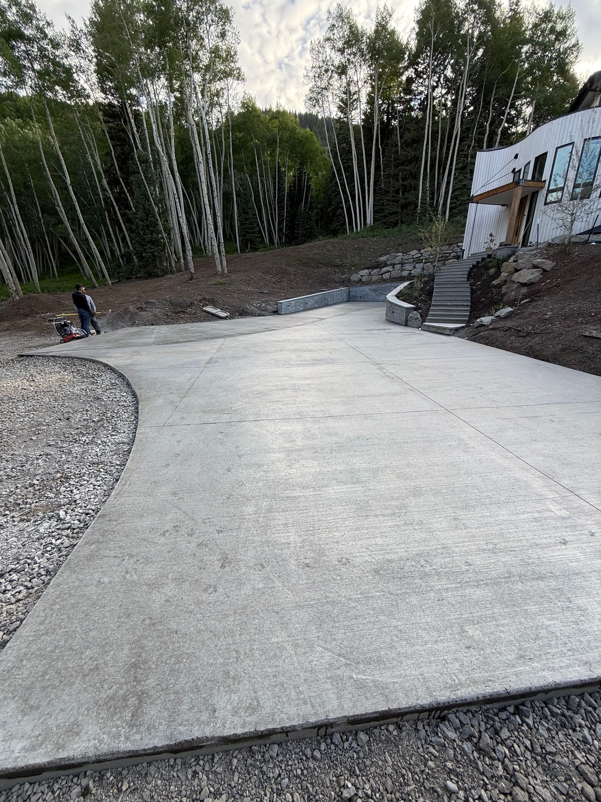 Concrete driveway with gravel edges and retaining wall, leading to a building under construction.