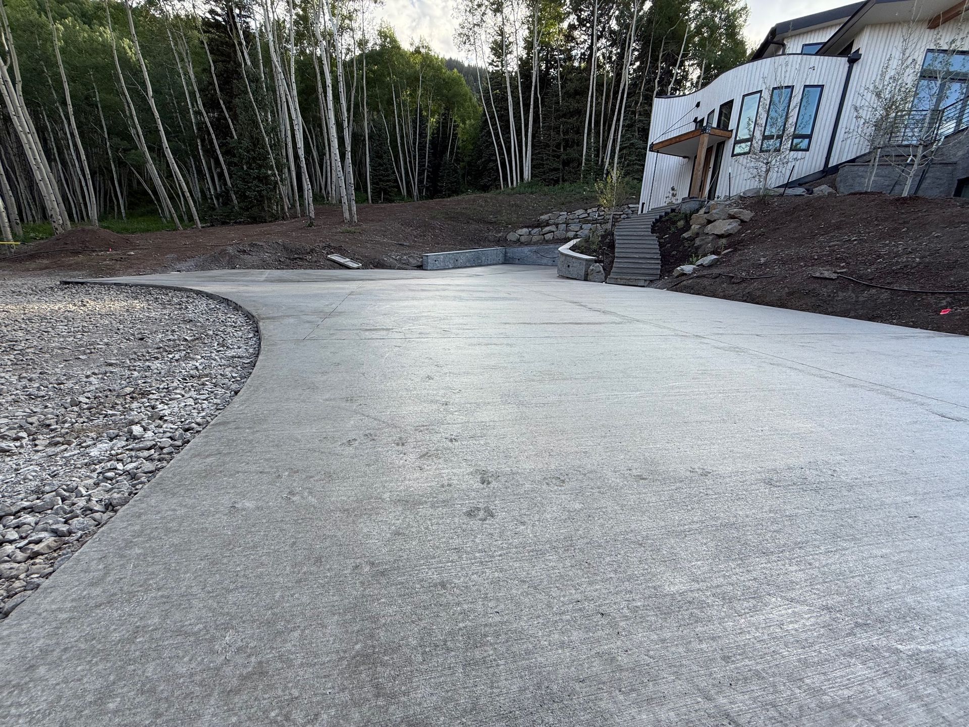 Concrete driveway curves toward a house, bordered by gravel and trees.