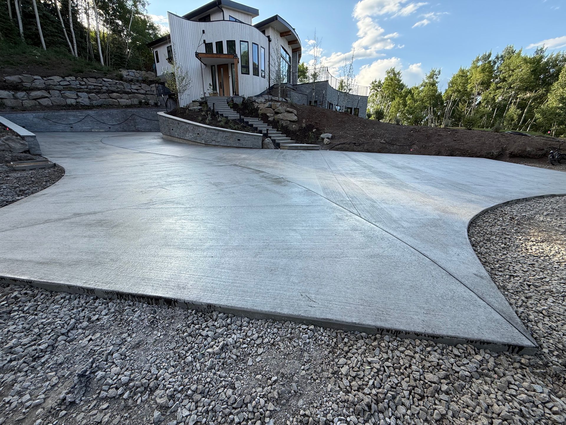 New concrete driveway leading up to a modern, multi-story house on a hillside.