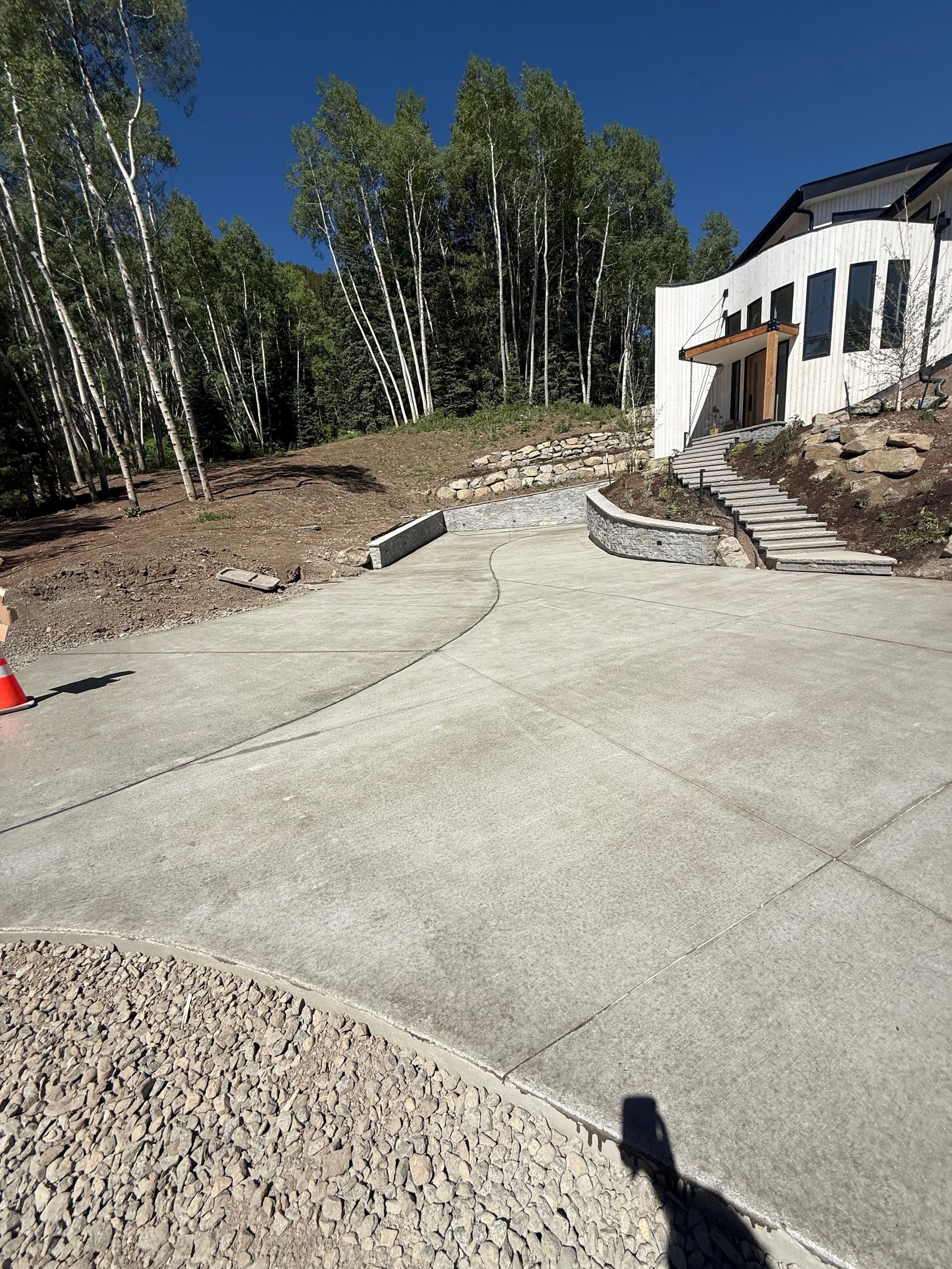 Concrete driveway leading up to a white house with arched windows and a wooden door; trees and blue sky.