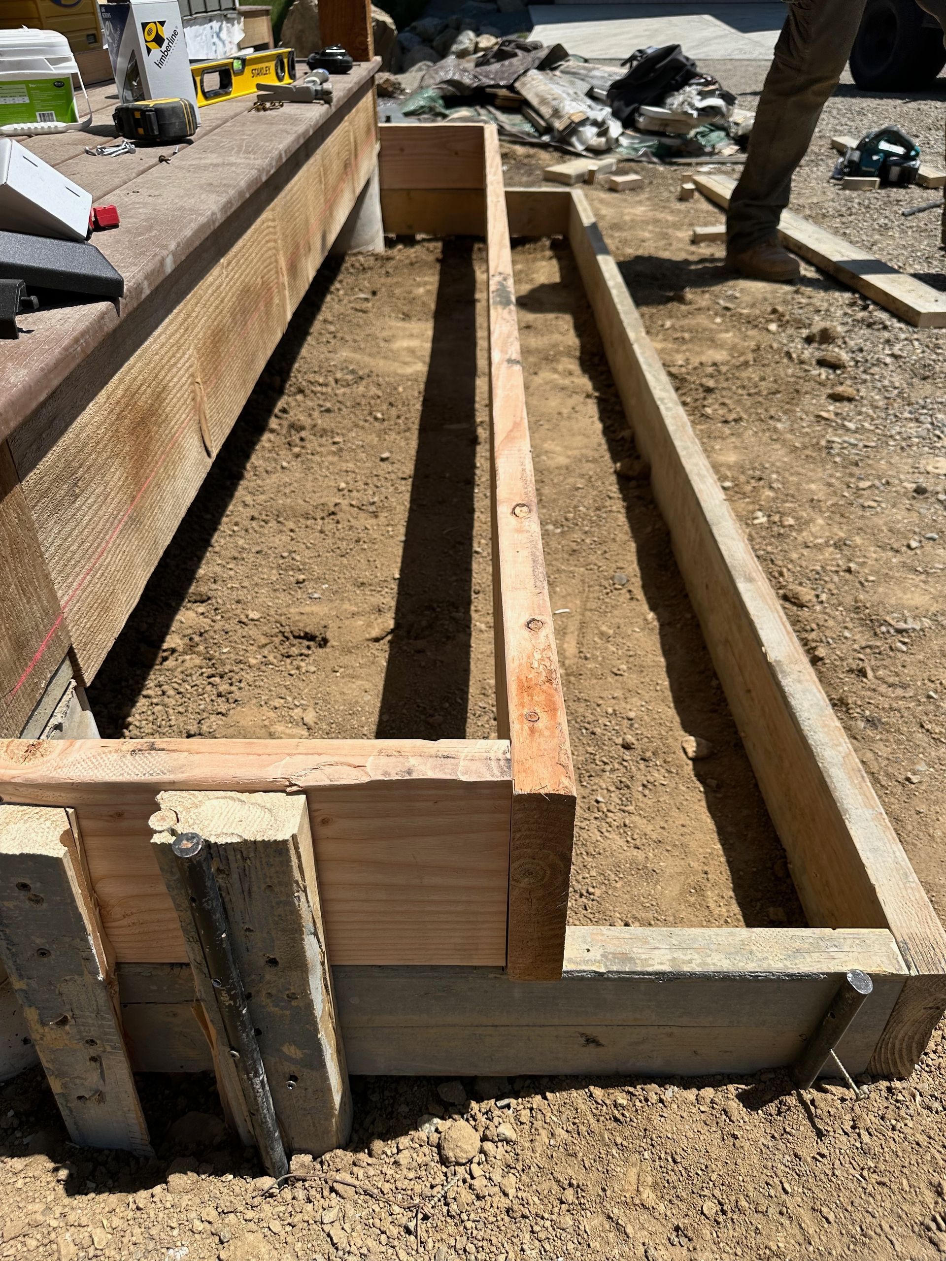 Wooden forms on a construction site, filled with soil, next to a concrete structure.