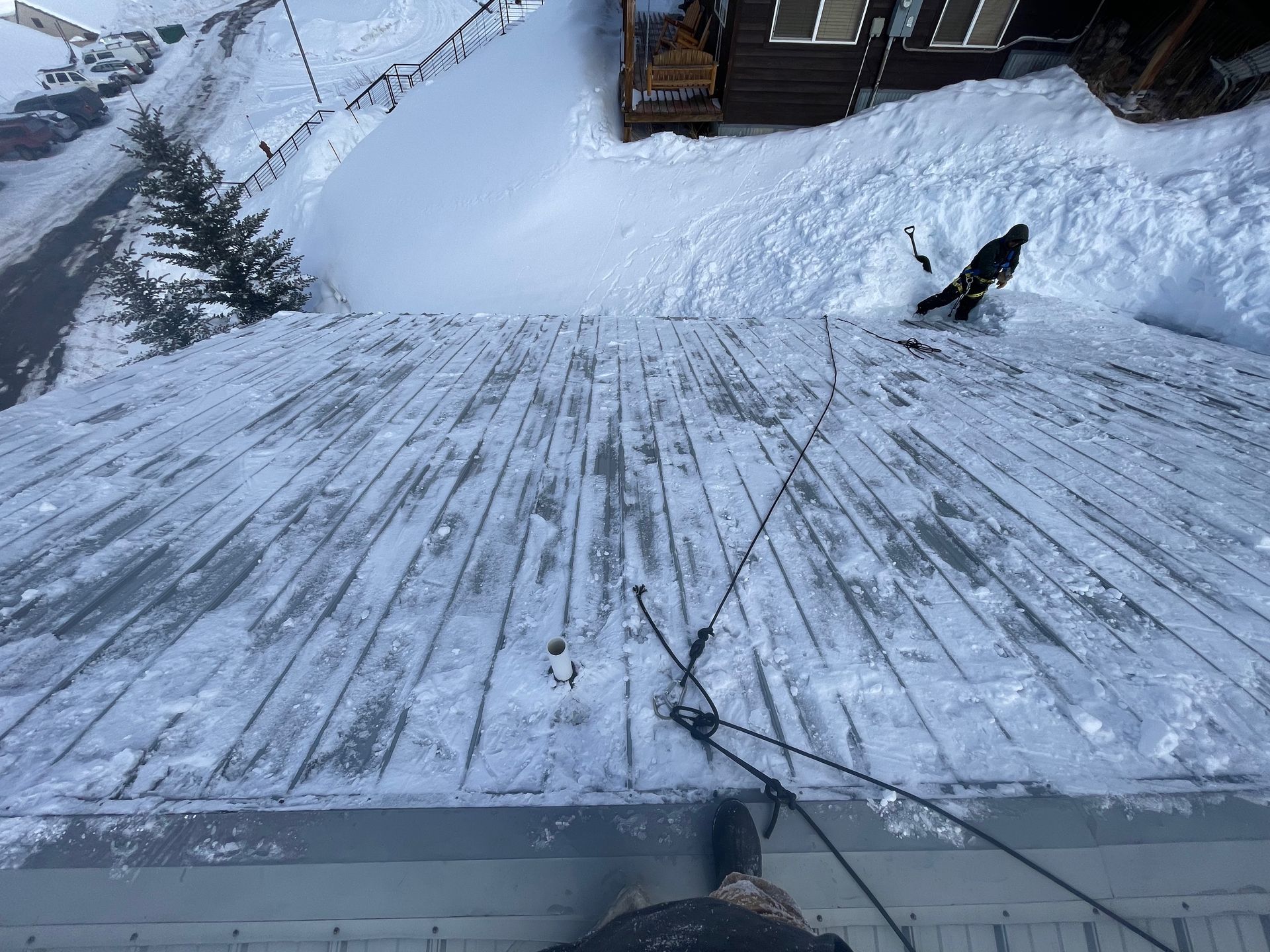 Snow-covered rooftop, person shoveling snow, cables, snow-covered ground, house, outdoor.