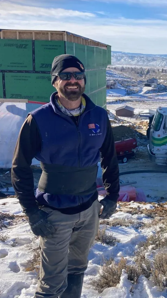 Man in winter construction site, wearing beanie, sunglasses, blue vest,