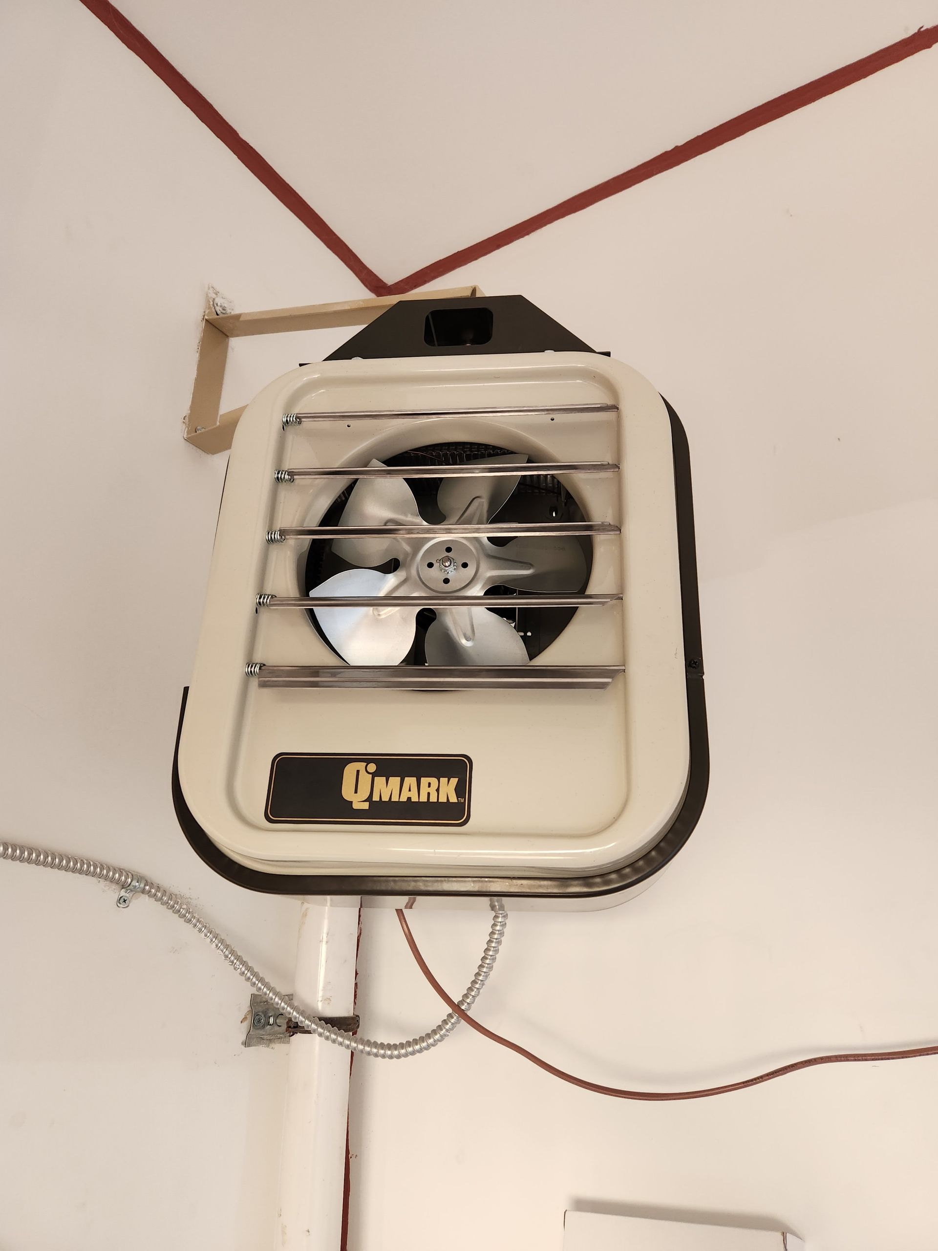 Off-white wall-mounted fan with protective grill and black accents; wooden bracket attached to wall.