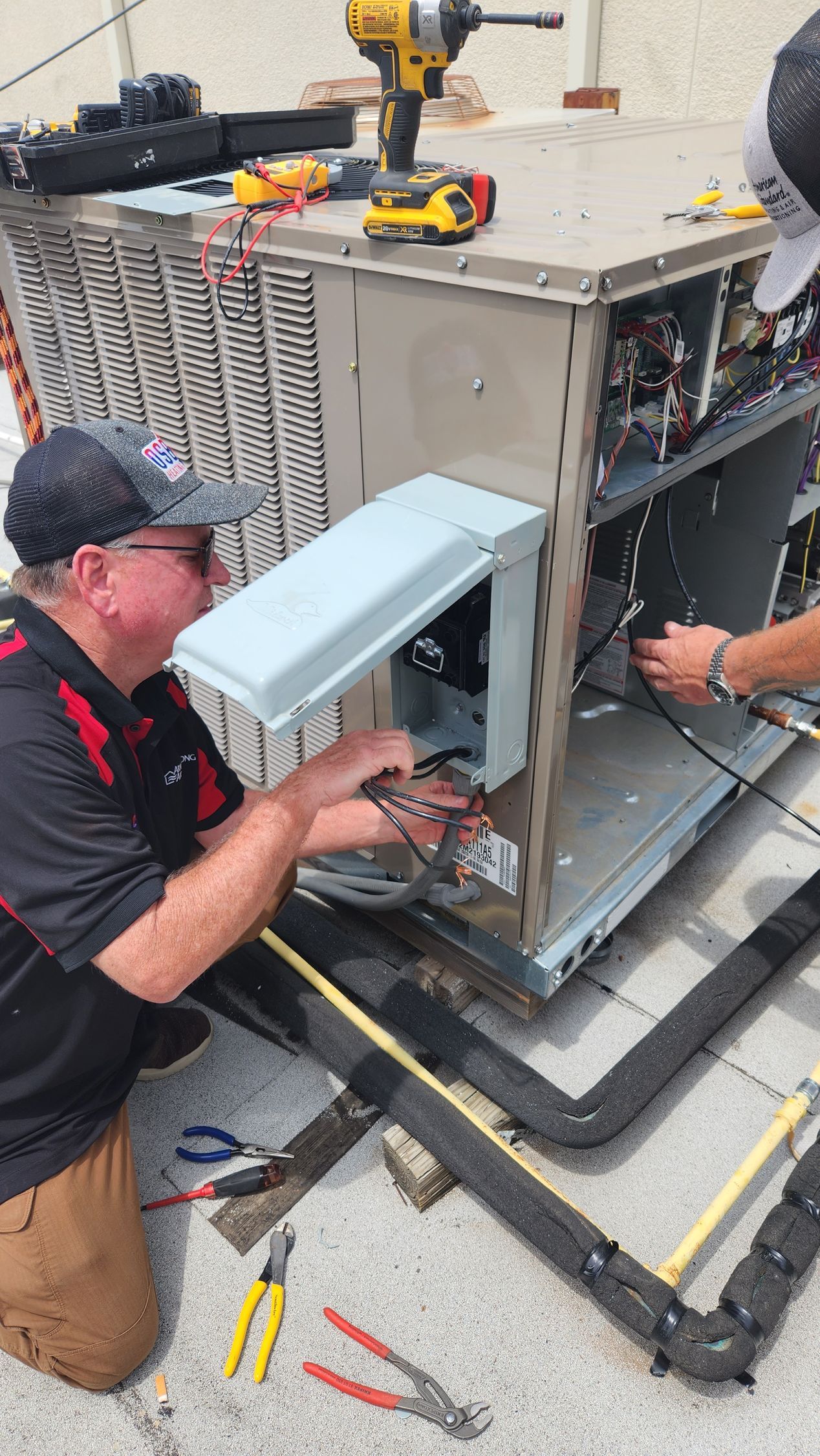 Two HVAC technicians repairing an air conditioning unit on a rooftop.