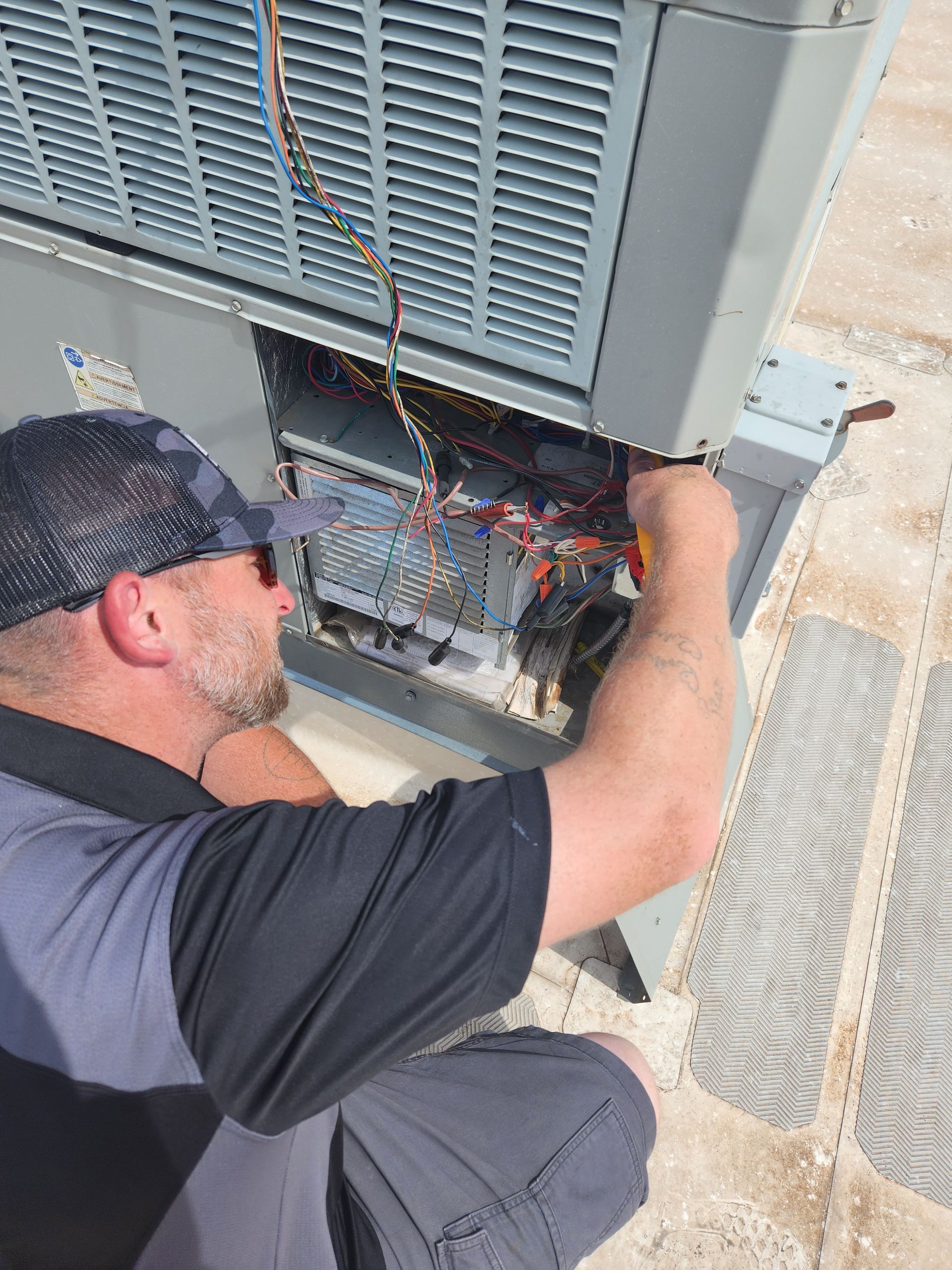 Person in hat, working on AC unit's electrical components on rooftop.