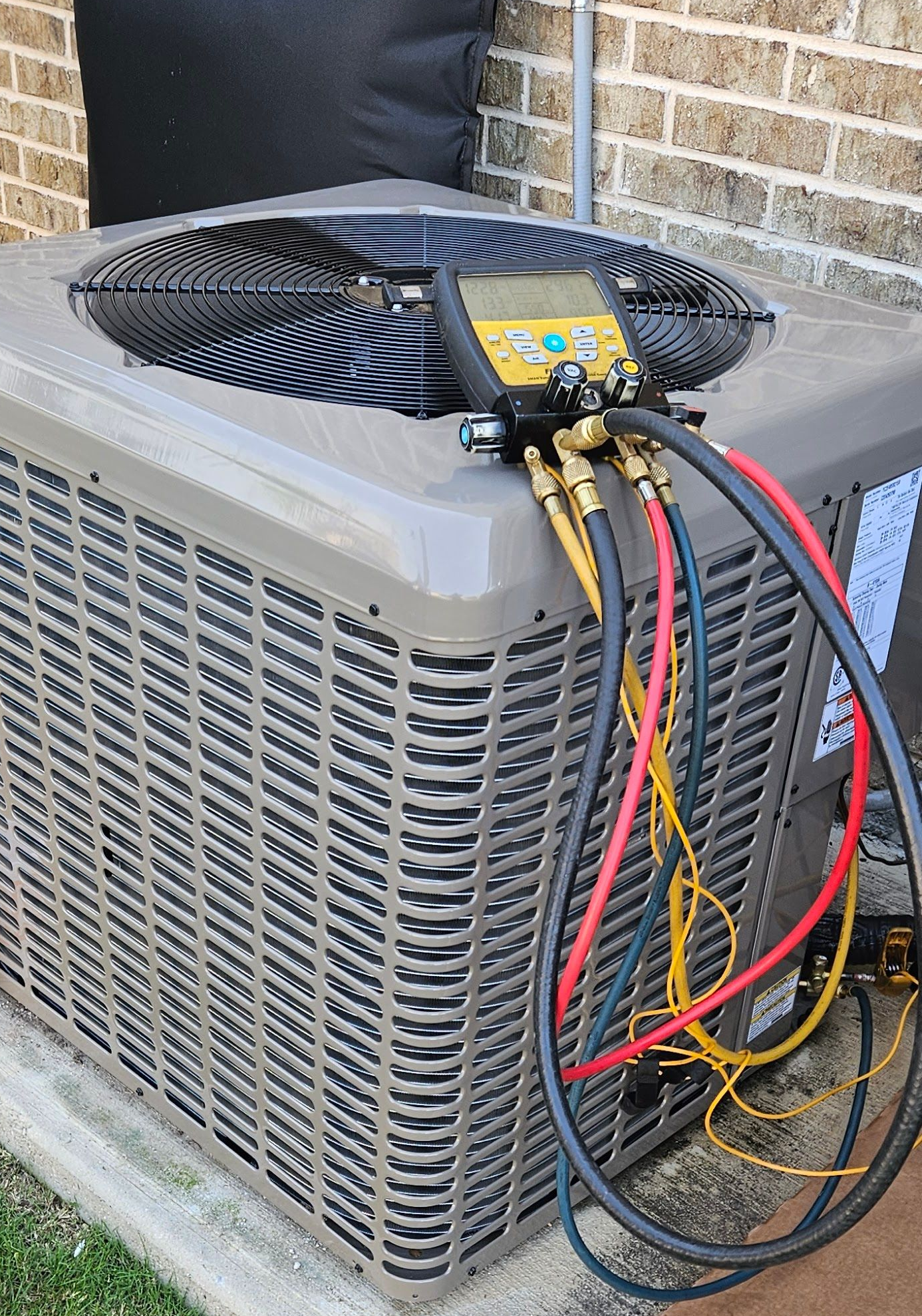 An air conditioning unit being serviced outdoors, with gauges attached.