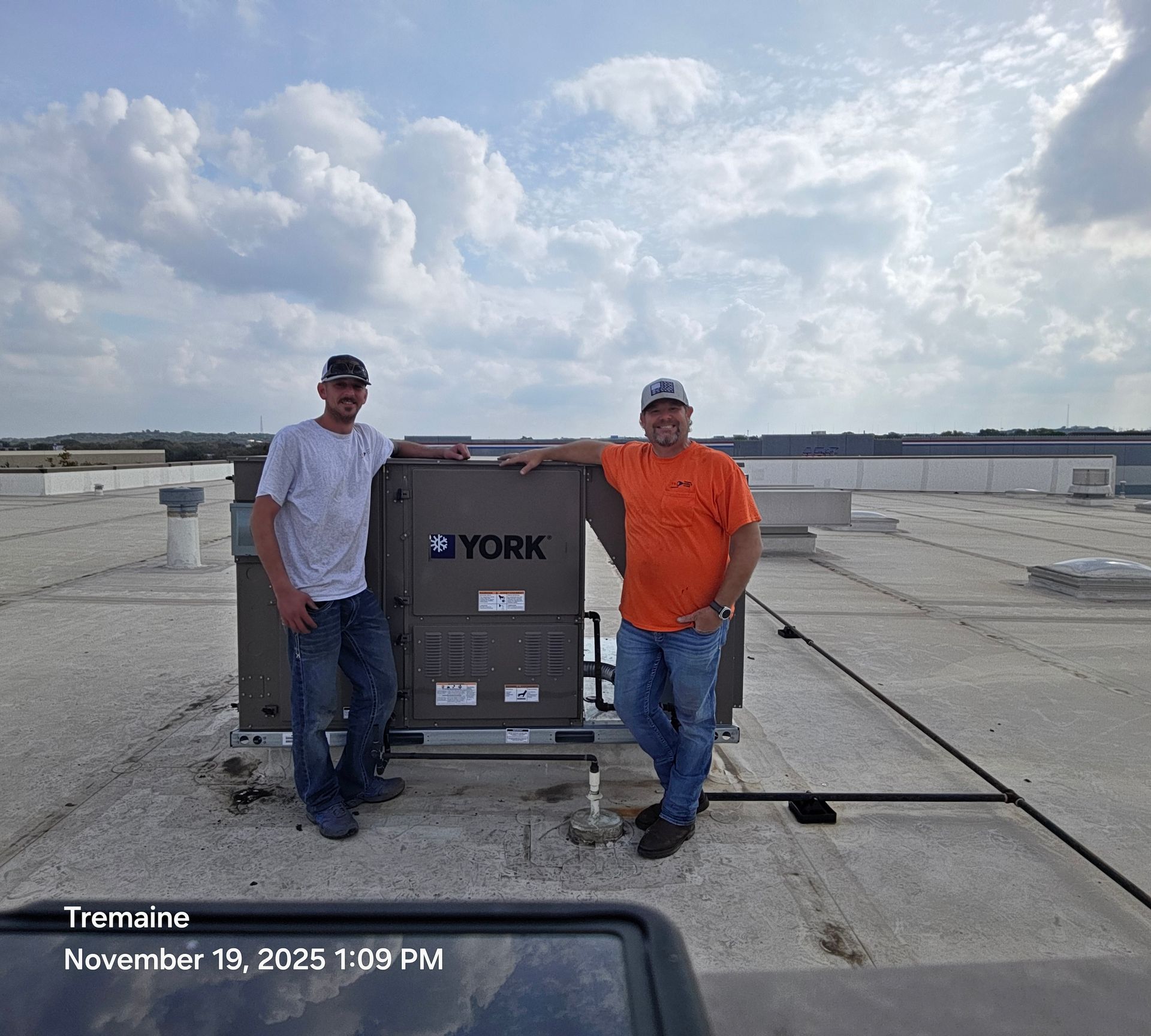 Two men standing on a rooftop next to a York HVAC unit. Overcast sky.