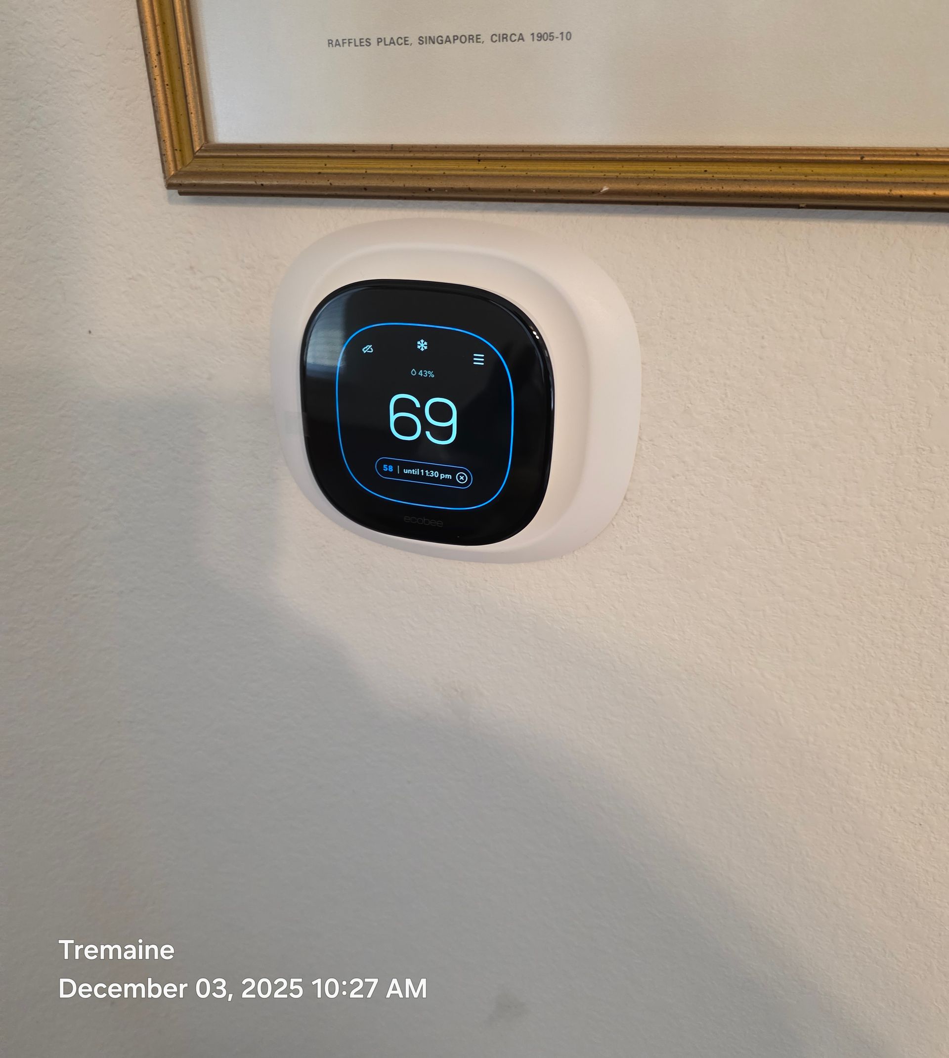 White smart thermostat displays 69 degrees, mounted on a wall under a picture frame.