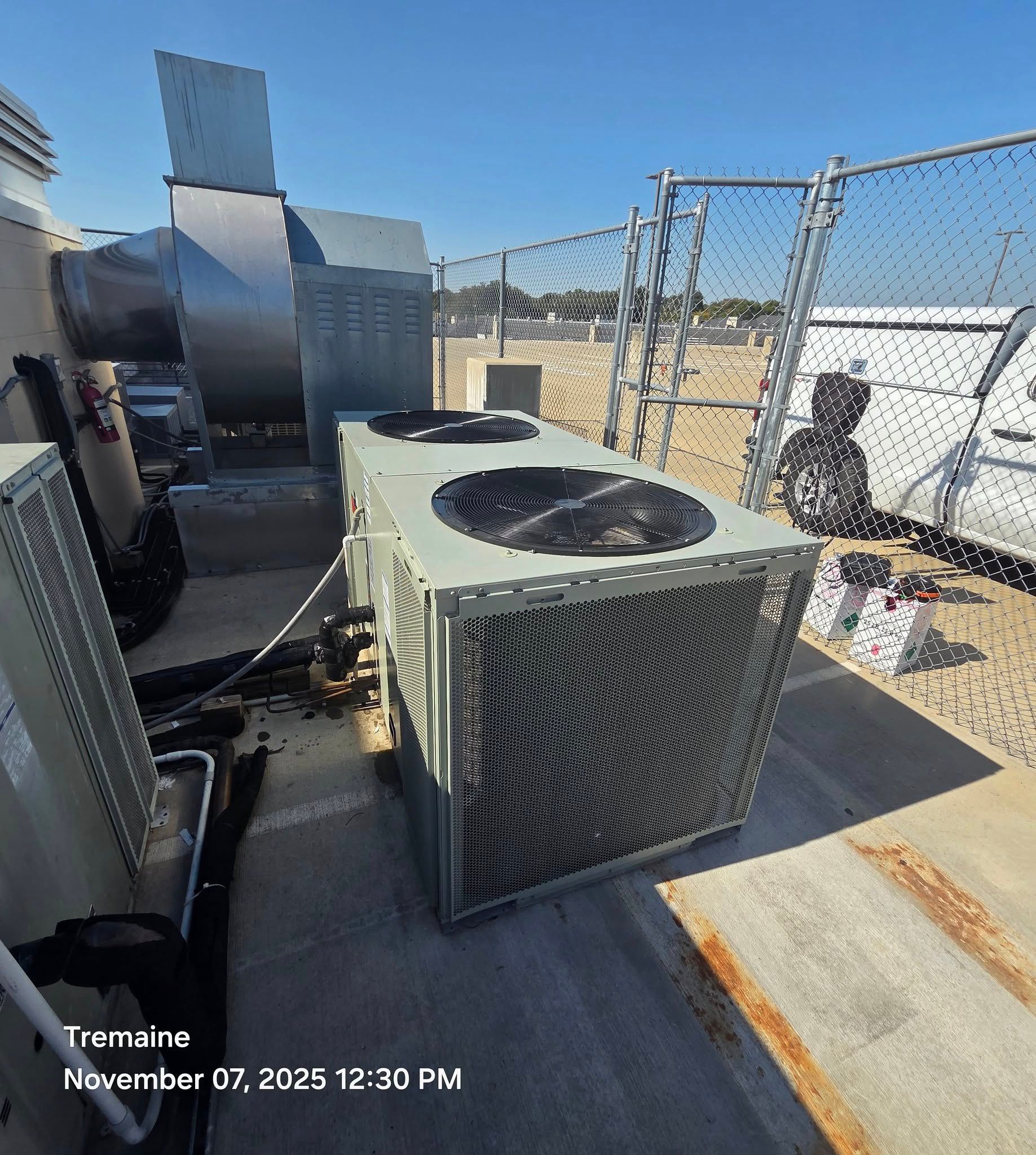HVAC unit on a rooftop with exhaust vents and a chain-link fence. Person in the background.