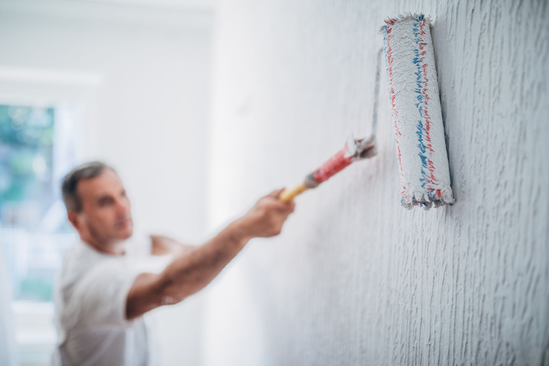 A man is painting a wall with a paint roller.