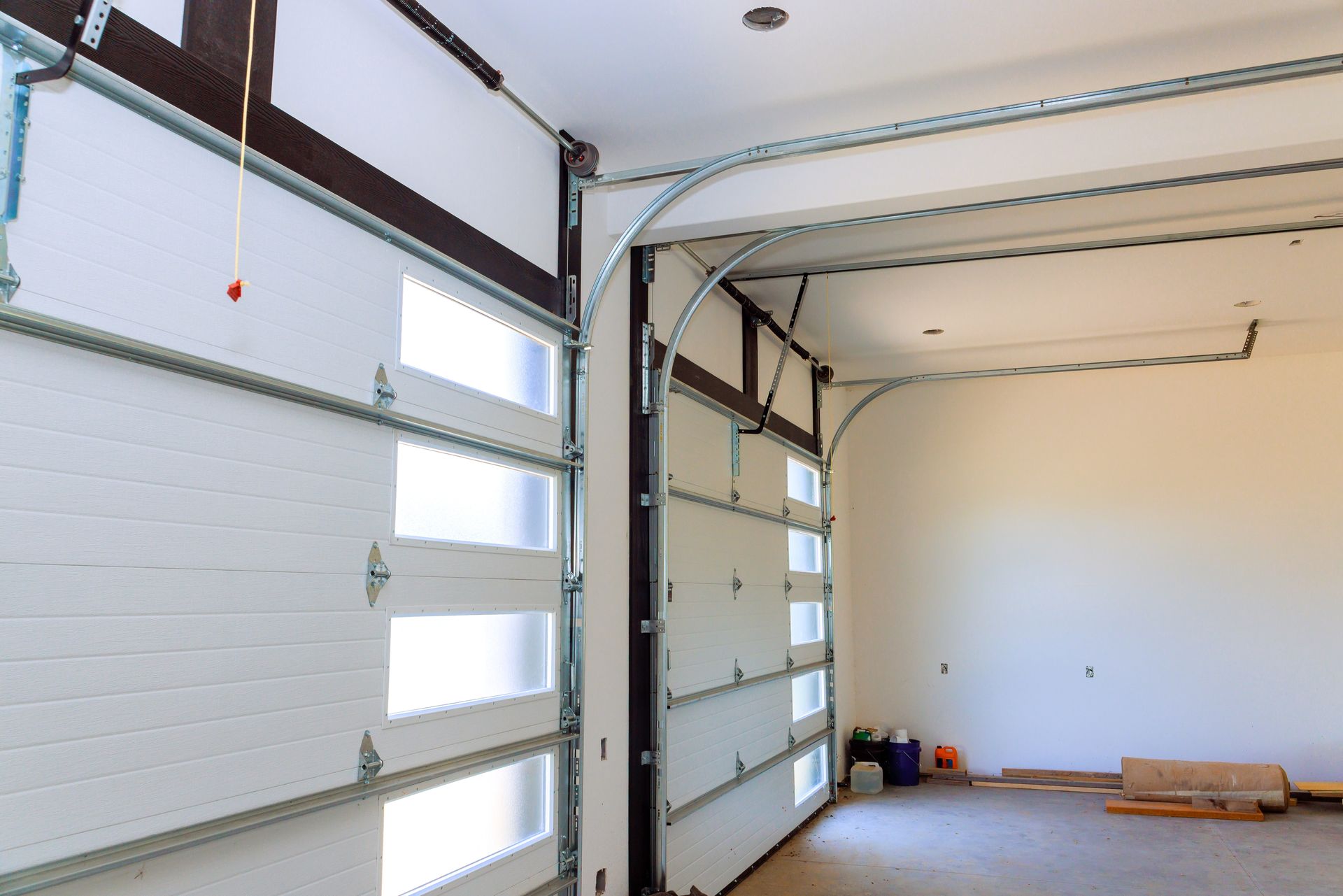 Open white garage door with glass panels; interior view of a room under construction.