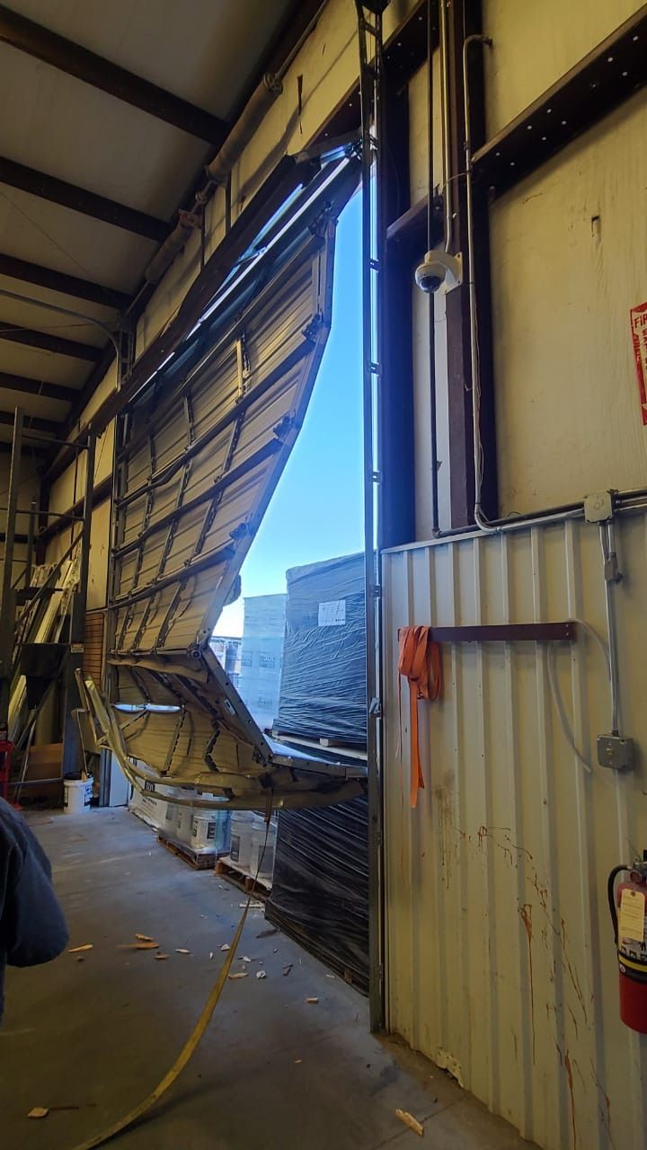 Damaged warehouse door, open. Metal panels are bent and torn, revealing the outside.