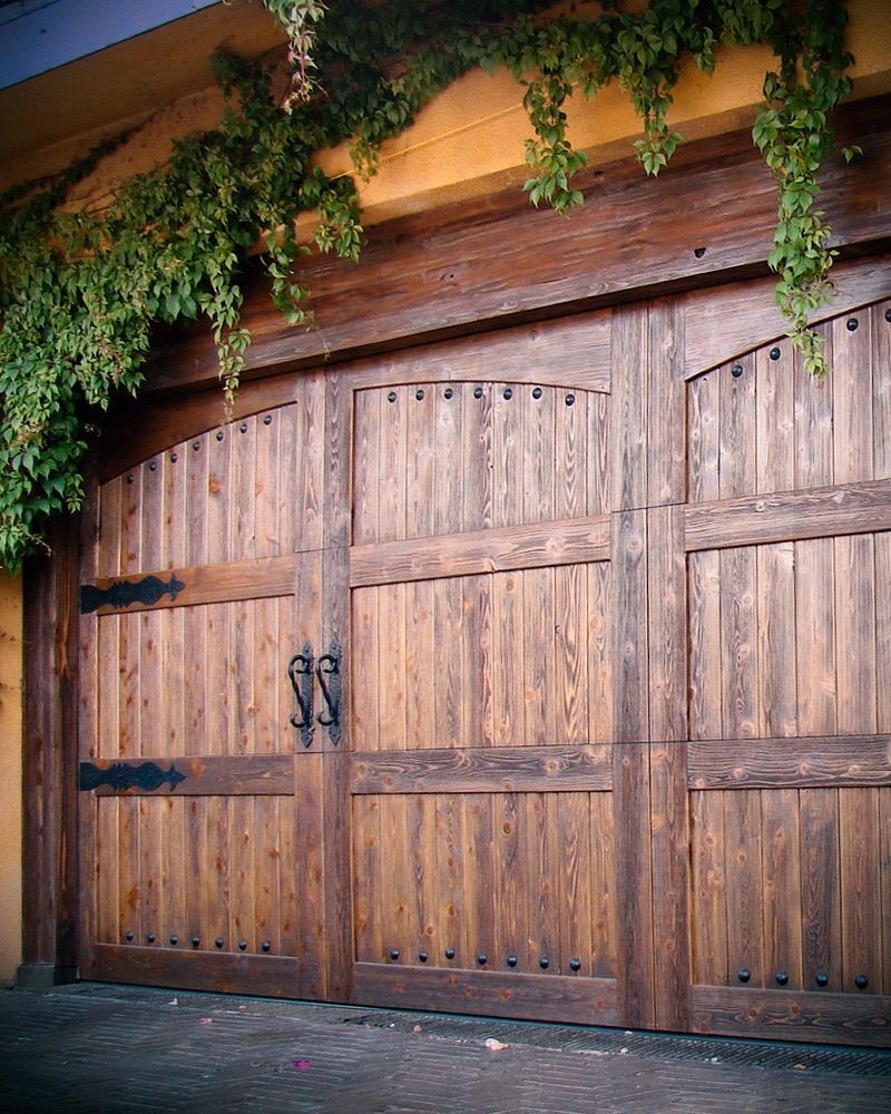Wooden carriage garage doors with dark hardware and ivy above.