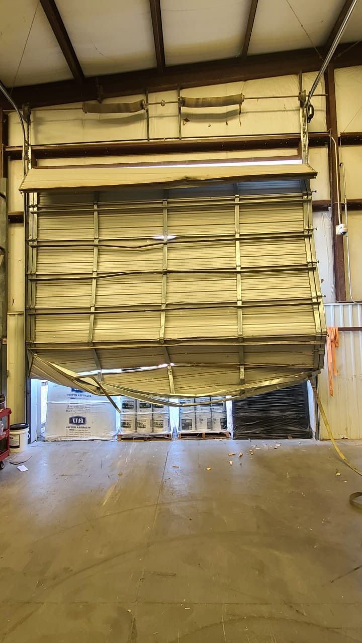 Damaged warehouse overhead door, partially open, with exposed contents.