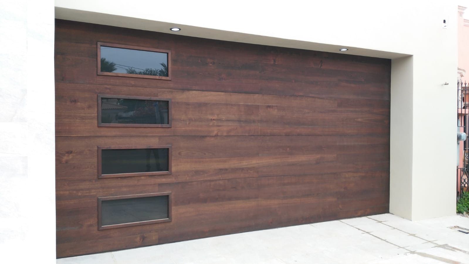 Dark wood garage door with four rectangular windows, set in a white exterior.