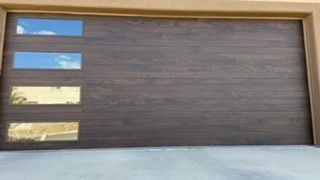 Brown garage door with three horizontal windows reflecting sky and surroundings.