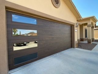 Brown garage door with three rectangular windows, next to a tan house.