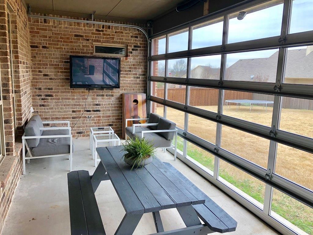 Outdoor patio with brick wall, glass garage door, seating, TV, and picnic table.