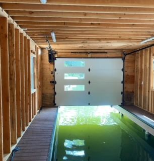 Garage door open to a pool; interior view. Wood-framed walls and ceiling. Green water in the pool.