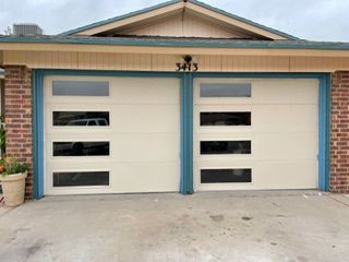 Two beige garage doors with rectangular windows, flanked by brick and teal trim.