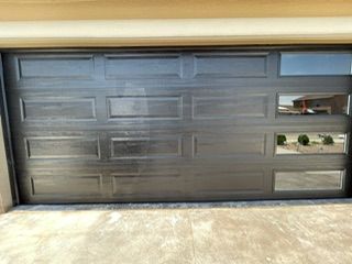 Black garage door with glass windows; sunlight reflects on the surface.