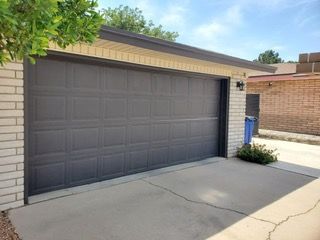 Gray garage door on a brick building with a concrete driveway and small green plants.