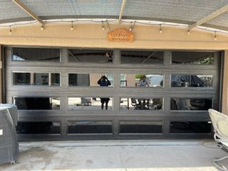 Gray garage door with multiple glass panes reflecting a person and outdoor setting.