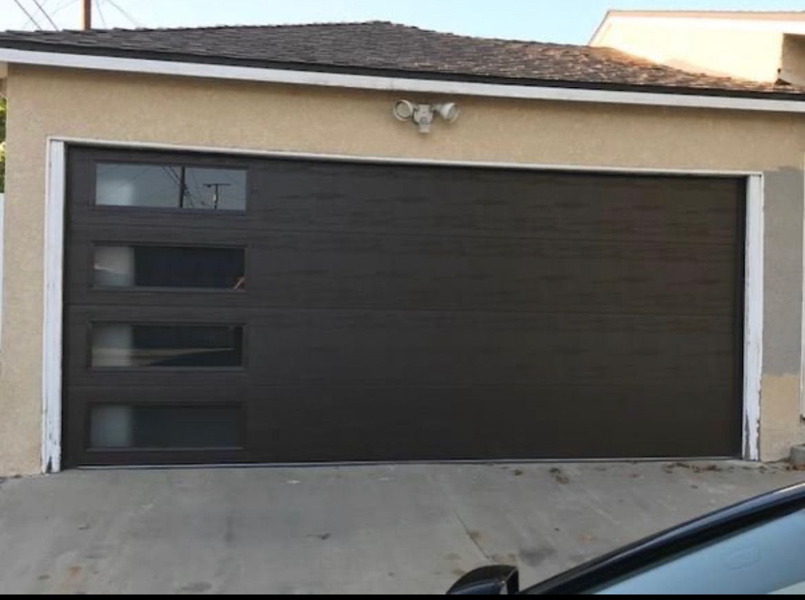 Brown garage door with windows, on a tan building. Concrete driveway.