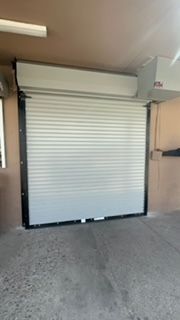 Rolling metal security door, silver and black, closed. Mounted in concrete opening.
