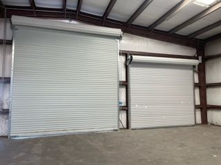 Two closed, gray, rolling steel warehouse doors inside a building with a metal frame and a gray floor.
