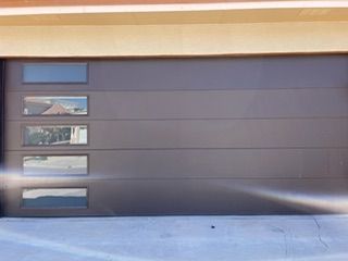 Modern gray garage door with four horizontal panels and rectangular windows.