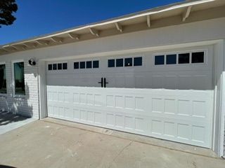 White garage door with rectangular windows, black handles, and a concrete driveway.