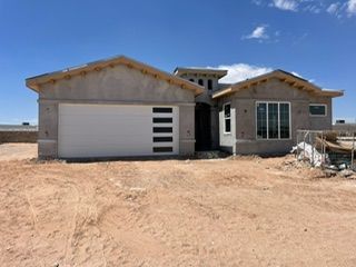 New construction home exterior, stucco walls, garage door, windows, unfinished, desert setting.