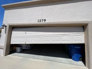 Garage door partially open, revealing contents inside and blue trash bin. House number 