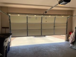 Garage door partially open, revealing a concrete floor and beige walls. A black trash can is visible.
