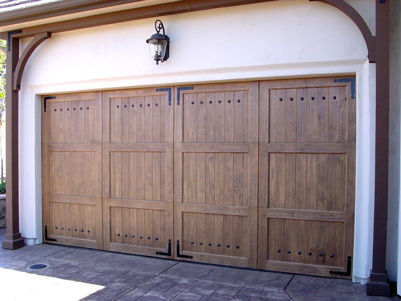 Wooden garage doors with decorative black hardware under a white facade and arched entryway.