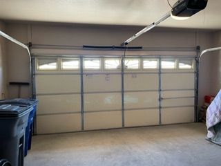 Garage interior with a closed white garage door. Black trash bins are on the left.