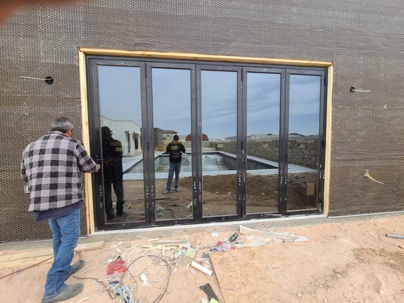 Person installs black folding door with mirrored glass; exterior of a building with visible pool in reflection.