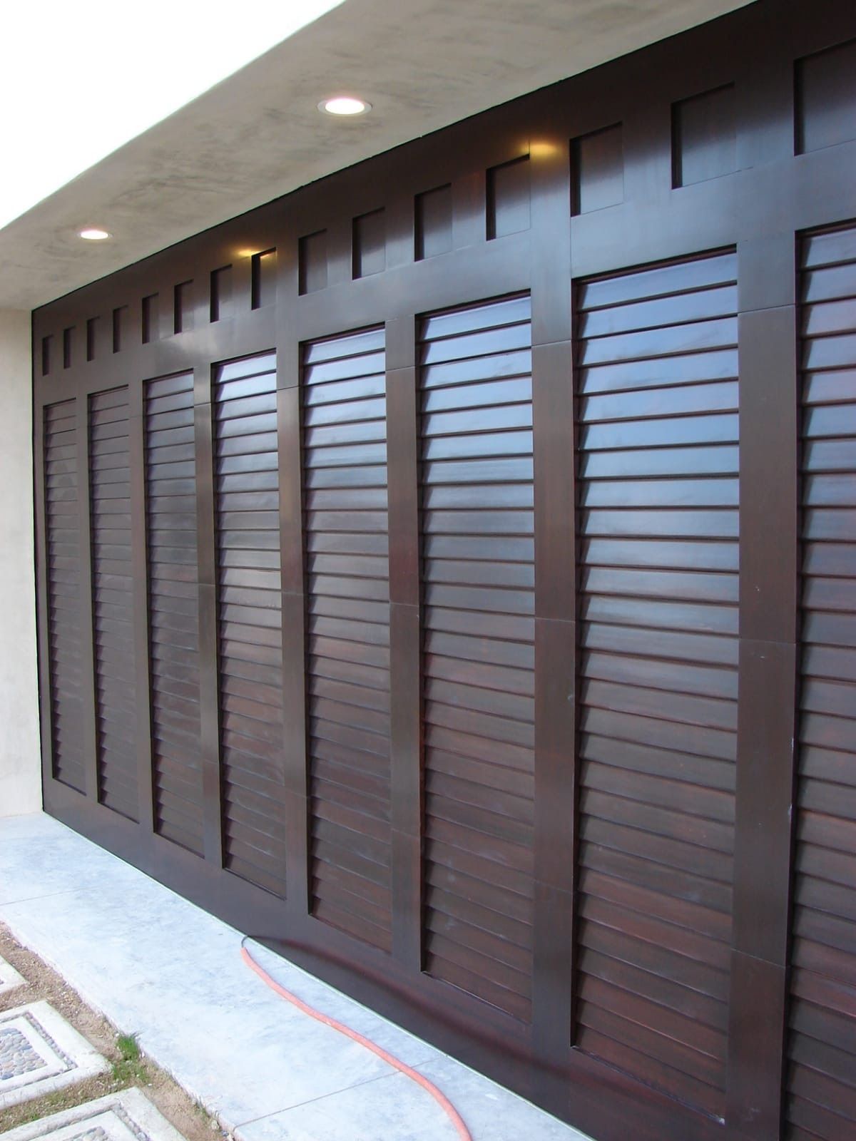 Dark wood garage door with horizontal slats, vertical frame, and top accent lights.